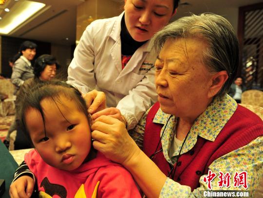 图为胡木英亲手给听障儿童戴上助听器。 翟羽佳 摄