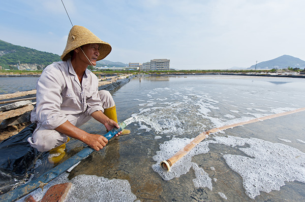 有30多年从业历的盐民阿飞正在引海水入盐池,这是晒盐开始的步